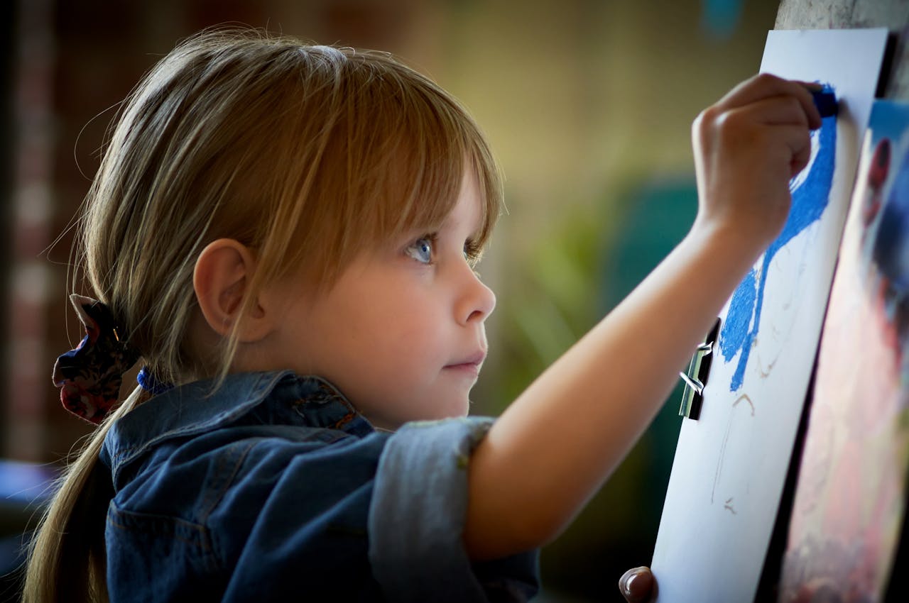 A young girl focuses intently while painting on an easel, showcasing creativity and concentration.